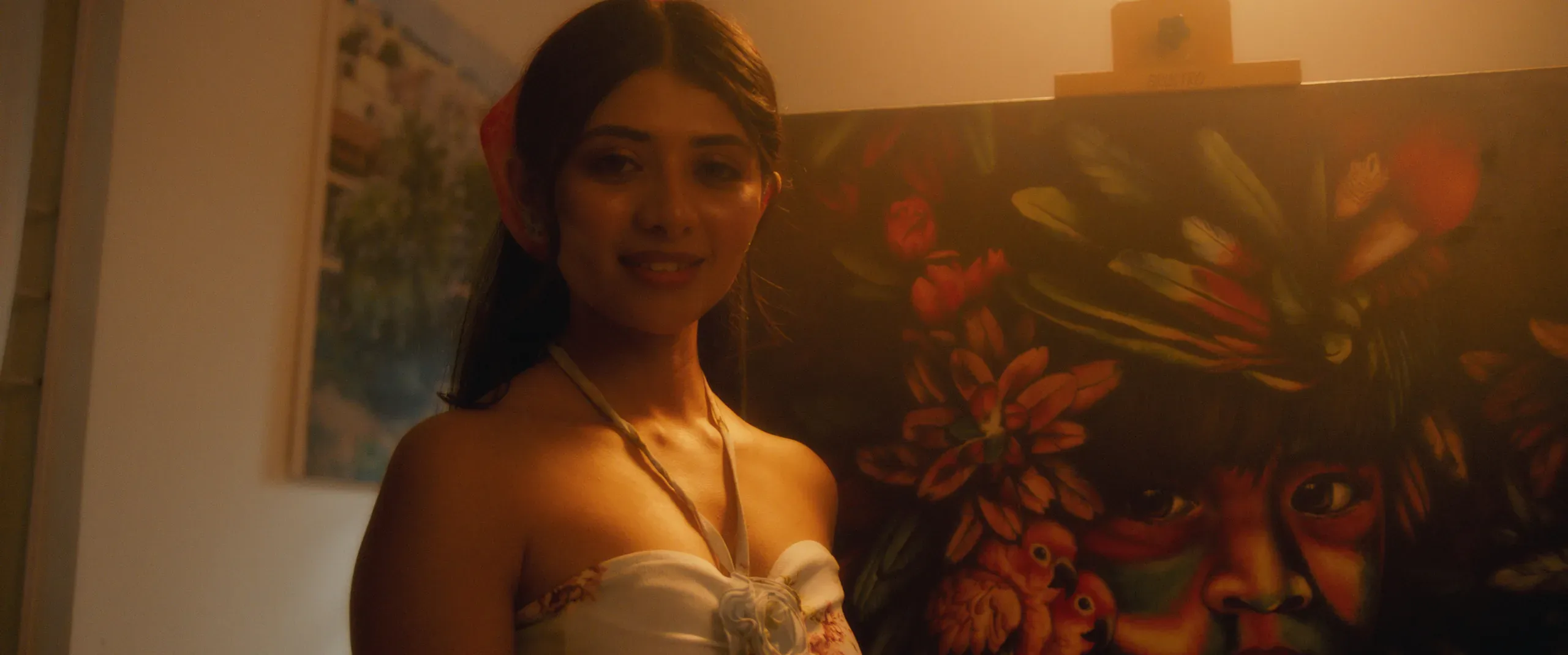 Warm close-up of a smiling woman before a vivid floral painting, bathed in golden light.