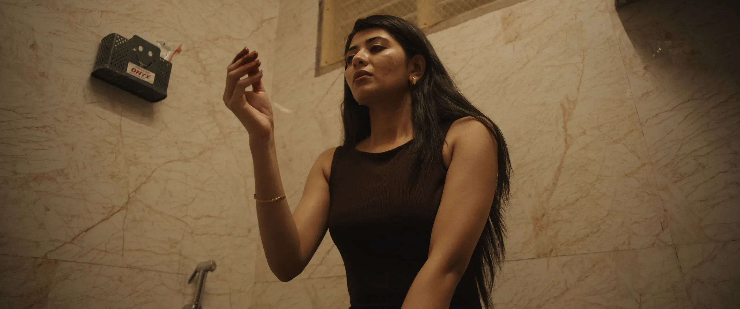 A woman reaches toward a switch on a marble wall, seen in profile under warm light.