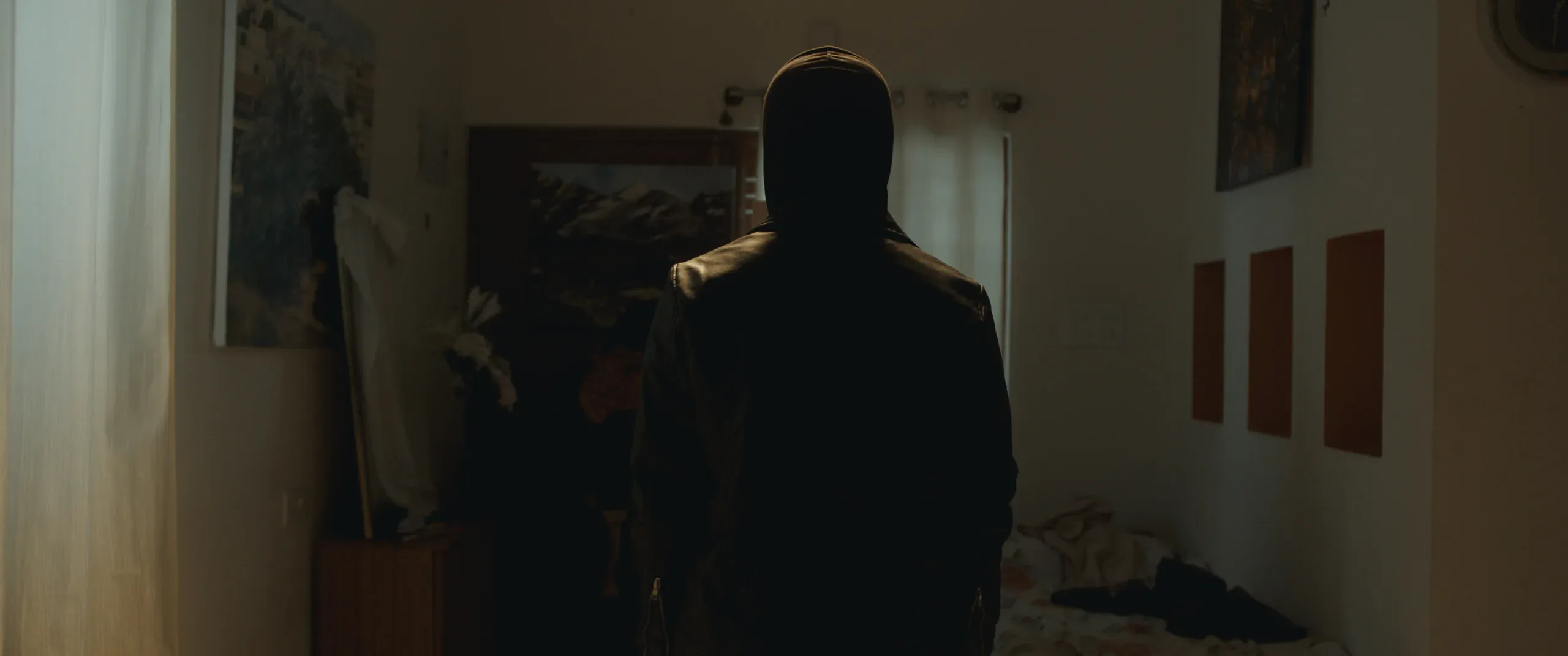 A dark silhouetted figure stands in a brightly lit bedroom doorway.